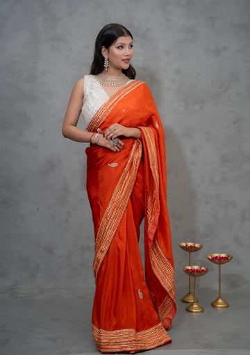 H.O. silk saree with golden striped border and kundan-style stone embroidery, available in red, orange, green, yellow, wine, and pink